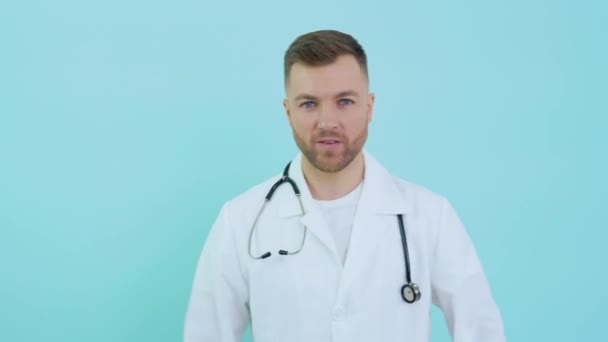Vrolijke succesvolle arts met stethoscoop in witte vacht op blauwe achtergrond tonen biceps — Stockvideo