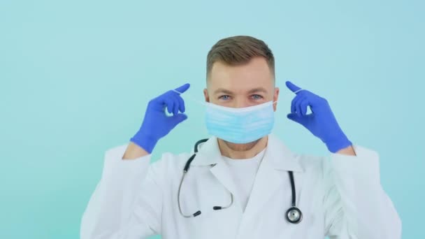 Lekarz zakłada niebieską maskę ochronną na niebieskie tło. Ochrona wirusów — Wideo stockowe