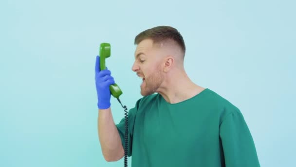 Medico arrabbiato in uniforme verde urlando in un vecchio telefono su uno sfondo blu — Video Stock