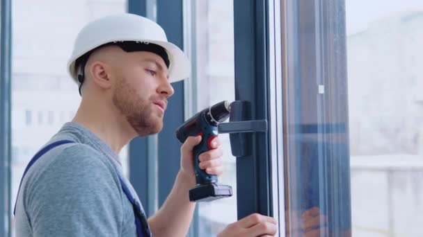 Master in een helm en een schroevendraaier installeert ramen — Stockvideo