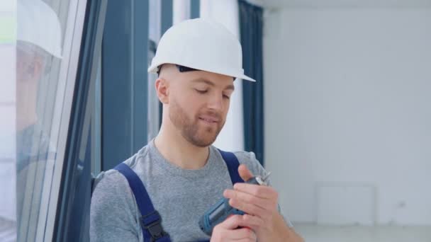Window installer with a screwdriver stands near the window — Vídeo de stock