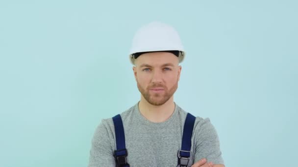 Serviceman in een helm en overall kijkend naar camera op blauwe achtergrond — Stockvideo