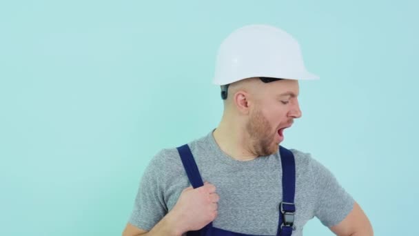 戴头盔和工作服的普通工人在蓝色背景下打呵欠 — 图库视频影像