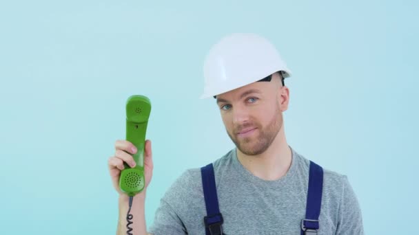 Ремонтник в комбінезоні і шолом тримає старий телефон в руках і вказує на нього — стокове відео