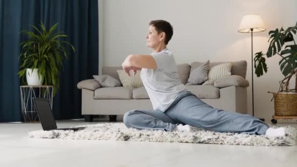Starsza kobieta robi ćwiczenia medytacyjne rozciągające sportową jogę. Jasny pokój w domu — Wideo stockowe