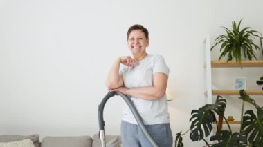 Temizlik yaparken elinde elektrikli süpürgeyle son sınıf bir kadının portresi. Oda temizliği rutini. Ev süpürgesi temizleyici.