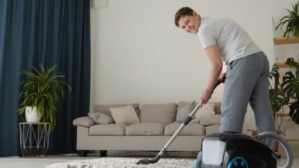 Senior woman vacuuming carpet at home. Housekeeping routine. Domestic hoover appliance cleaner — стоковое видео