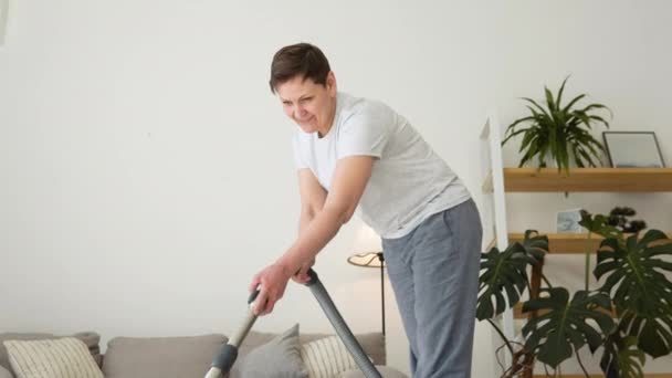 Senior woman vacuuming carpet at home. Housekeeping routine. Domestic hoover appliance cleaner — Vídeo de stock