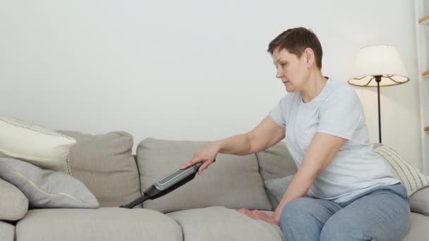 Senior woman vacuuming sofa manual vacuum cleaner — стоковое видео