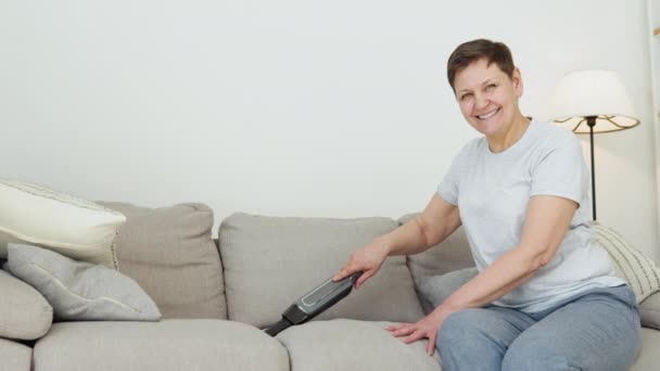 Senior woman vacuuming sofa manual vacuum cleaner — Vídeo de stock