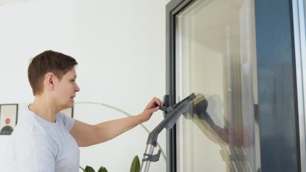 Senior woman cleaning window at home with a vacuum cleaner. Professional cleaning woman during work — Stock Video