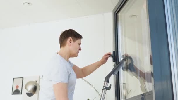 Mujer mayor limpiando ventana en casa con una aspiradora. Limpieza profesional mujer durante el trabajo — Vídeos de Stock