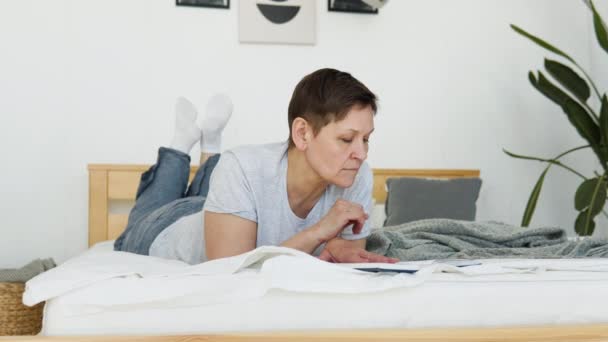 Pihent idős nő fekszik az ágyon, és könyvet olvas otthon — Stock videók