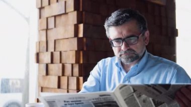 Son sınıf öğrencisi rahat bir kafede oturmuş gazete okuyor.