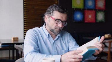 Yetişkin bir erkek kafede otururken kitap okur. Emekli dinleniyor.