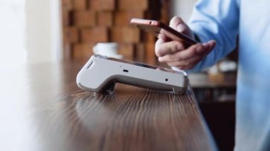 Kafedeki erkek müşterinin nakitsiz cüzdanında e-para. NFC teknolojisiyle ödeme yapan müşterinin erkek eli. Elektronik ödeme makinesi veya kart okuyucu üzerinden cep telefonuyla satın alma