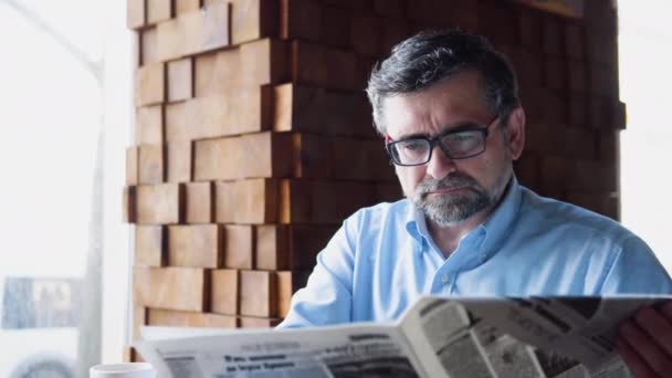 Senior man reads a newspaper sitting in a cozy cafe — Vídeo de stock