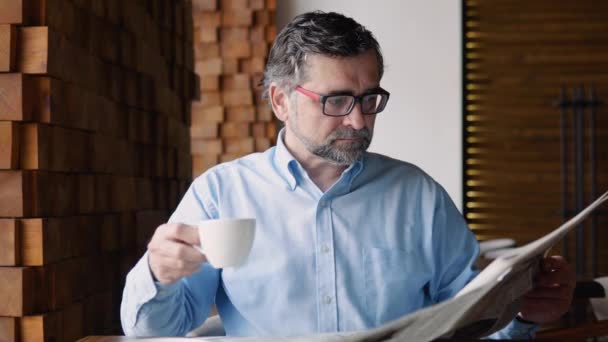 Старший мужчина проводит время в кафе, читает газеты и пьет кофе. — стоковое видео