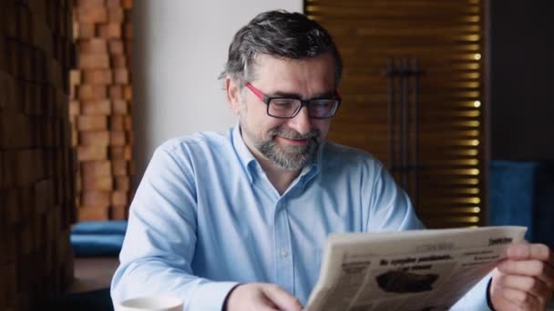 Senior man reads a newspaper sitting in a cozy cafe — Video