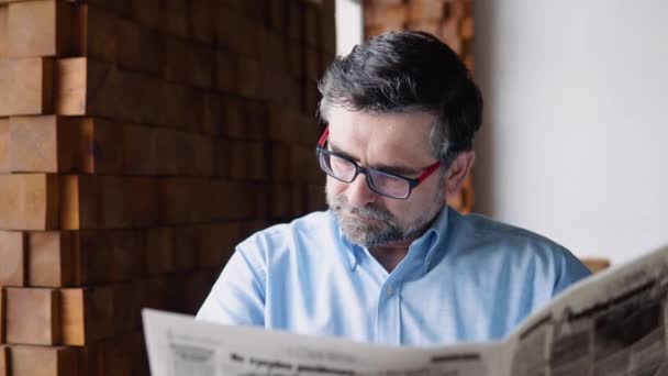 Ο πρεσβύτερος διαβάζει εφημερίδα καθισμένος σε ένα ζεστό καφέ. — Αρχείο Βίντεο