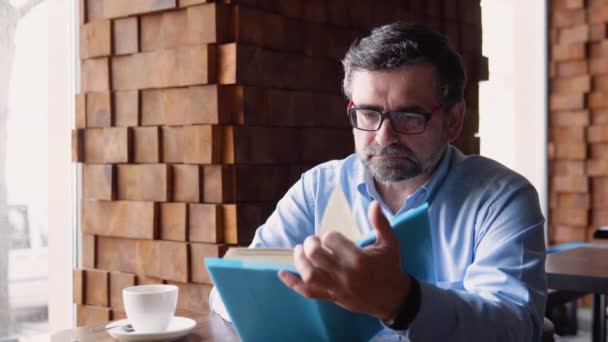 Glad stilig senior man läser en bok i café — Stockvideo