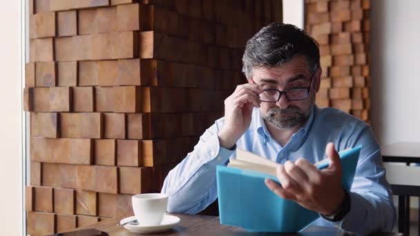 Gammal man läser bok medan han sitter på ett café. Pensionären vilar — Stockvideo