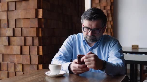 Senior man använder telefon när han sitter på ett café — Stockvideo