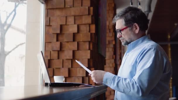 Senior man bestudeert documenten zittend in een café — Stockvideo