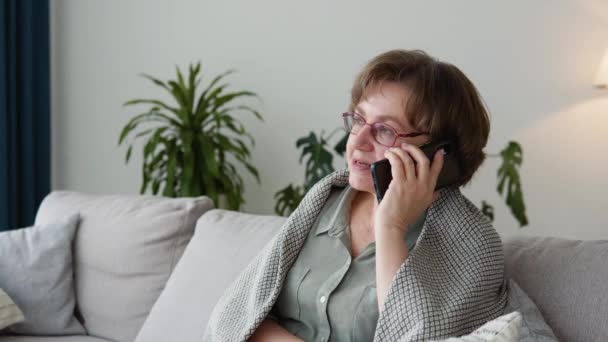 Happy senior woman relaxing on cozy sofa, talking on smartphone with friends — Vídeo de stock