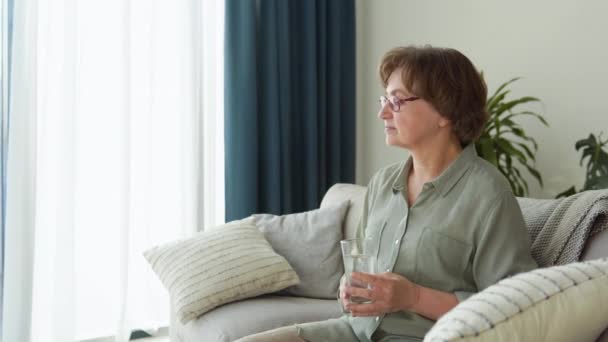 Bela senhora bebendo água sentada no sofá em casa — Vídeo de Stock