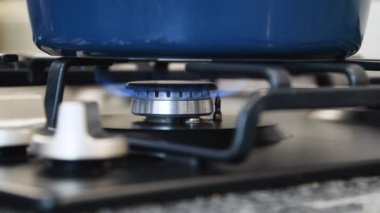 Gaz kesiliyor, yanan bir alev mutfakta mavi tencereli bir gaz sobası.
