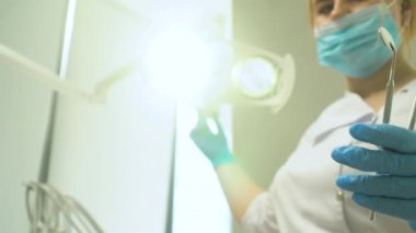 A female dentist turns on the lamp and coming closer to the patient holding tools