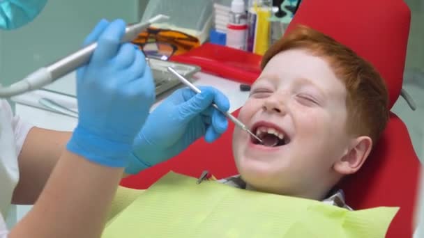 Szczęśliwy rudy chłopiec w recepcji u dentysty na krześle dentystycznym. Medycyna, stomatologia i koncepcja opieki zdrowotnej. Bezpieczna stomatologia — Wideo stockowe