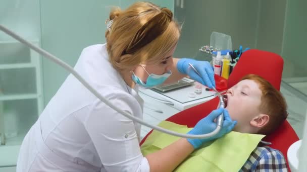 Niño pelirrojo en recepción en dentista en silla dental. Odontología pediátrica — Vídeos de Stock