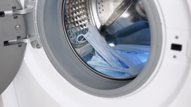 Erkek el, tıbbi maskeleri çamaşır makinesine koyar. Çamaşır makinesi yükleniyor. Çamaşır yıkama — Stok video