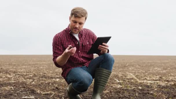 Fermier sur un champ avec une tablette avant de planter des cultures agricoles étudie l'état du sol — Video