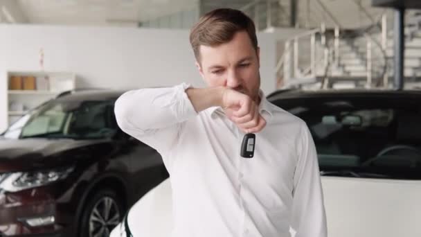 Portrait of happy adult successful man posing in auto showroom buying new automobile. Positive male smiling for camera and demonstrating keys while standing near new vehicle in showroom — стоковое видео