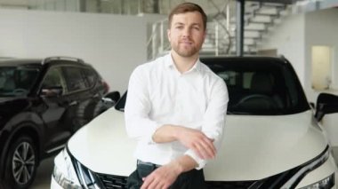 Araba galerisinde yeni bir arabanın yanında genç bir adamın portresi.