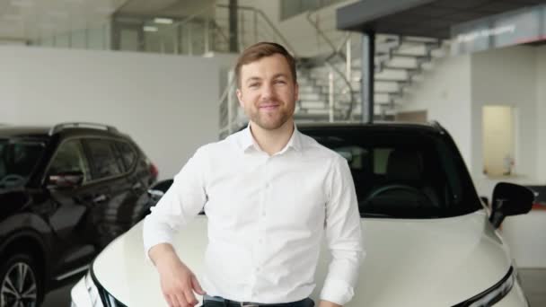 Portrait of a young man near a new electric car in a car dealership — Vídeos de Stock