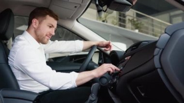 Adam yeni arabanın işlevlerine hoş bir şekilde şaşırdı. İş adamı satın almadan önce aracı inceliyor. Araba al.