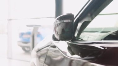 Unfolding the outside rearview mirror with built-in turn signal light on a prestigious brown car in a dealer showroom