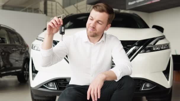 A man with keys rejoices in buying a new car in a car dealership — стоковое видео