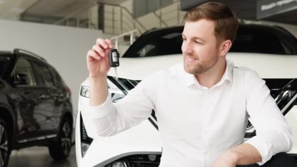 En man med nycklar glädjer sig åt att köpa en ny elbil i en bilhandlare — Stockvideo