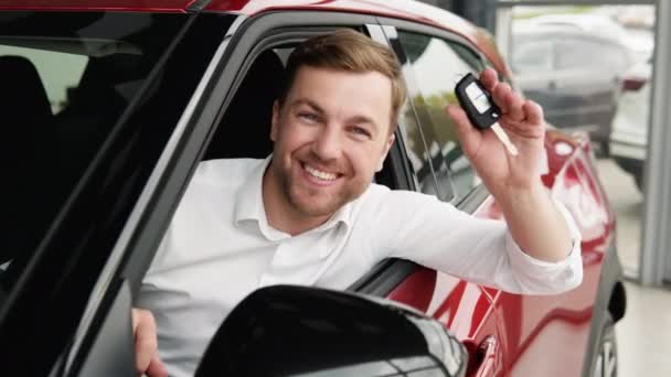 Happy man sits in new car in shop dealership and celebrate purchase of new vehicle. The man with keys shows emotions of happiness while driving in her new car — Vídeos de Stock