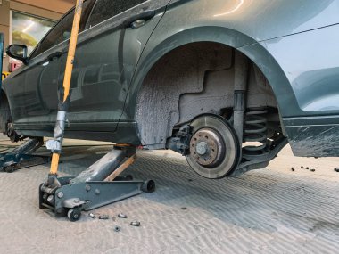 Hydraulic floor jacks under a gray car without a wheel in the car workshop