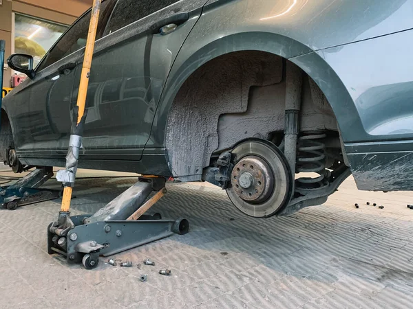 Araba atölyesinde tekerleği olmayan gri bir arabanın altında hidrolik zemin krikosu.