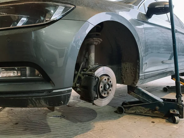 Hydraulic floor jacks under a gray car without a wheel in the car workshop. Car without tire need to be repaired Stockfoto