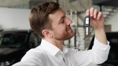 Bir adam araba galerisinde arabanın yanında video çekmekten mutlu olur.