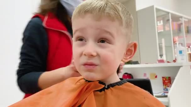 Cute blond uśmiechnięty chłopiec w fryzjera o fryzjera przez fryzjera. Ręce stylisty z narzędziami. Moda dla dzieci — Wideo stockowe