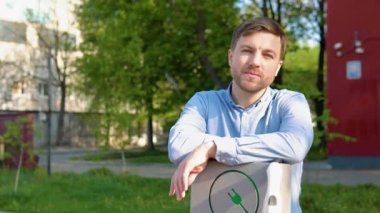 Şarj aletli bir adam şarj istasyonunda kameraya bakar.